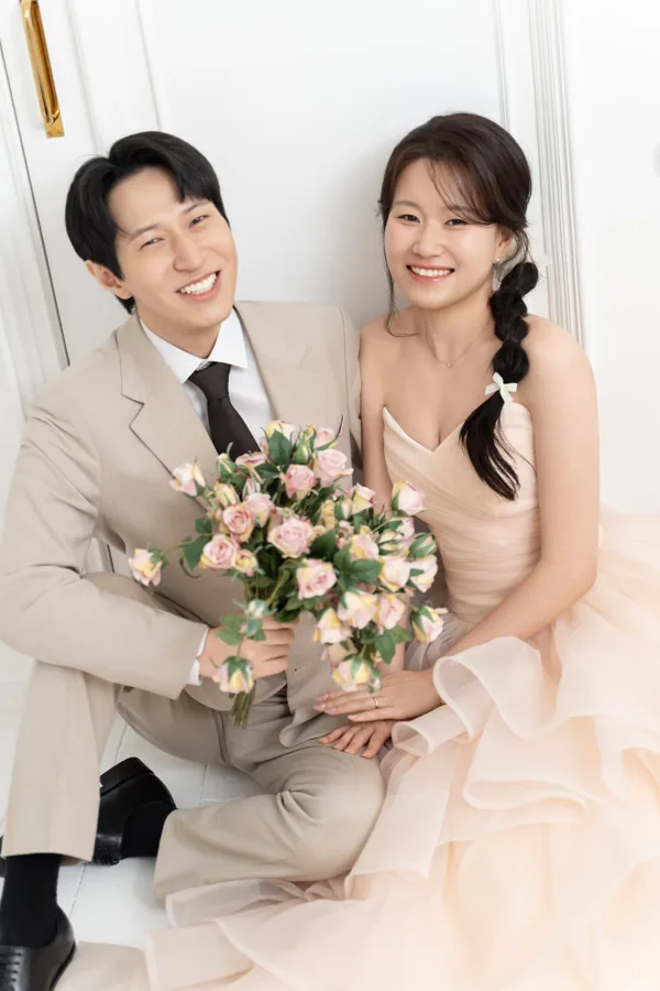 밝은 창가에서 꽃다발을 들고 환하게 웃는 두 사람